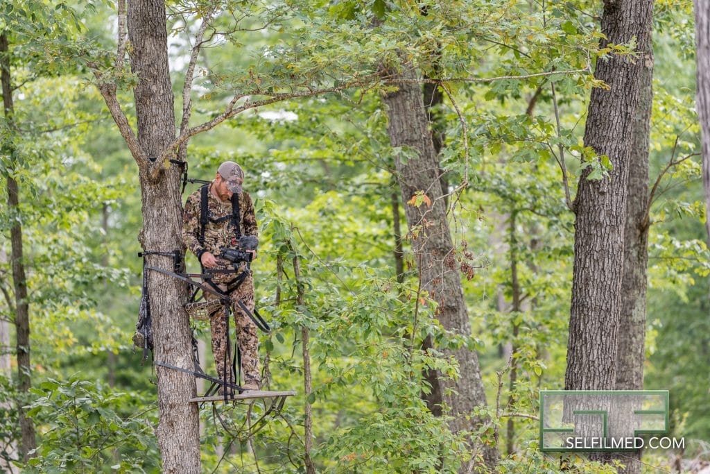 hunter in climbing treestand adjusting camera arm for self filming hunt